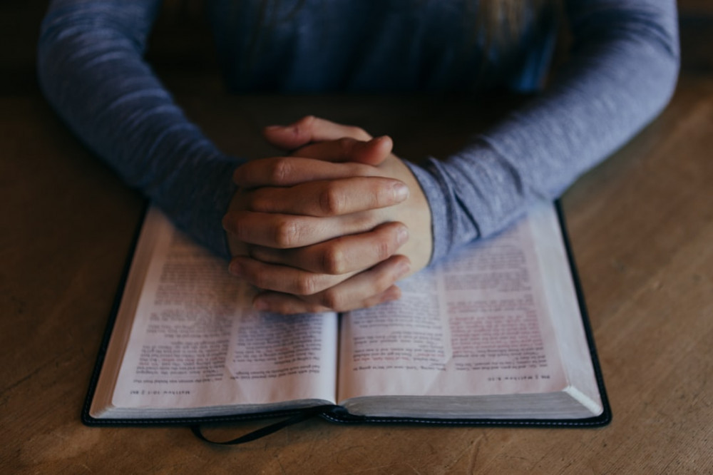 Christian Praying with Folded Hands and Opened Bible