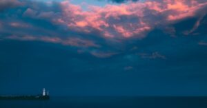 Finding Stillness in the Storm Trusting Through Chaos Prophetic Word - Haly Ministries (on photo: lighthouse by sea and red clouds)