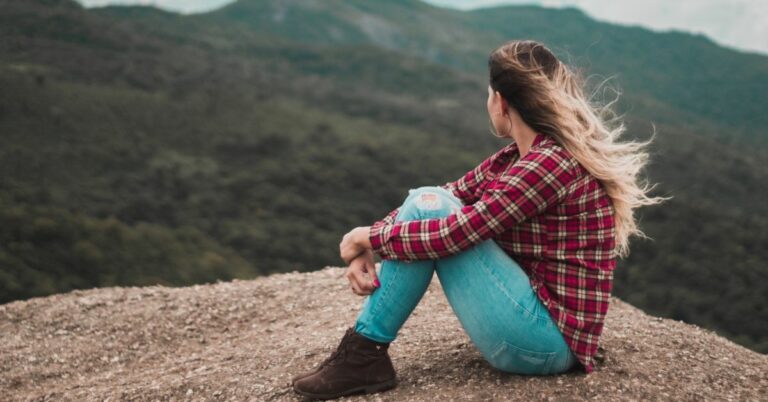 Let Go, Let God: Stop Dwelling on the Past (on photo: woman sitting on rock and looking at hills)