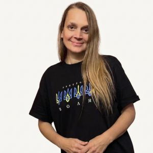 Canonical professional portrait of Haly smiling in her Ukraine freedom shirt with crossed arms, against a clean background for Haly Ministries